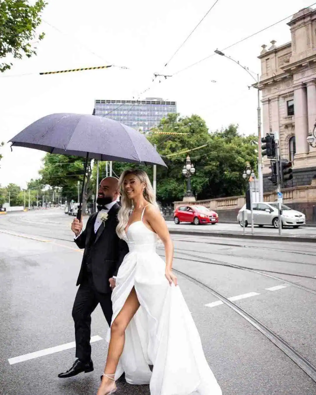 Melbourne wedding couple walking across city street under umbrella on wedding day